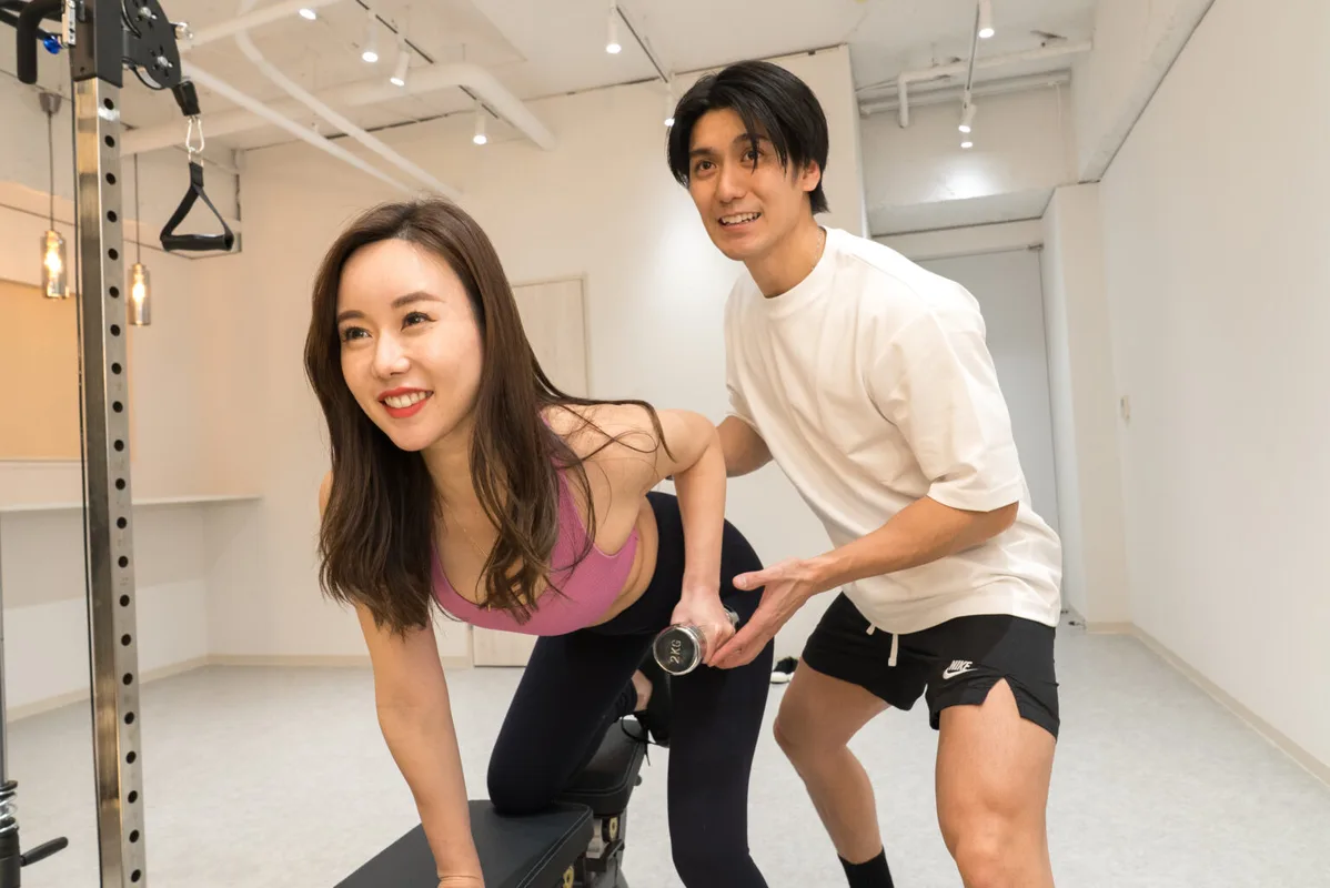 トレーナーがダンベルトレーニングをサポートしている様子